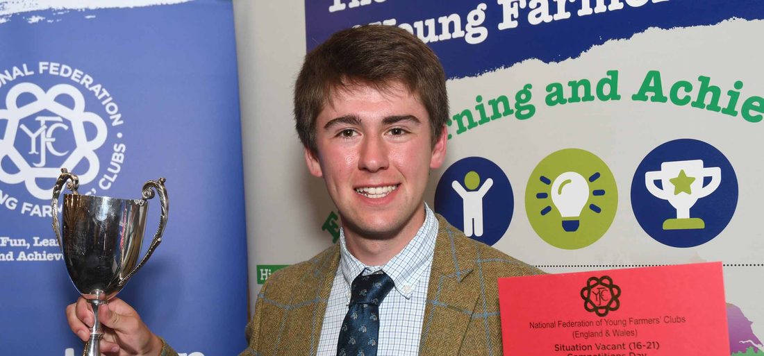 Jack holding the winner's cup and certificate for the Situations Vacant competition at the National Federation of Young Farmers' Clubs Competitions Day, in front of NFYFC banners.